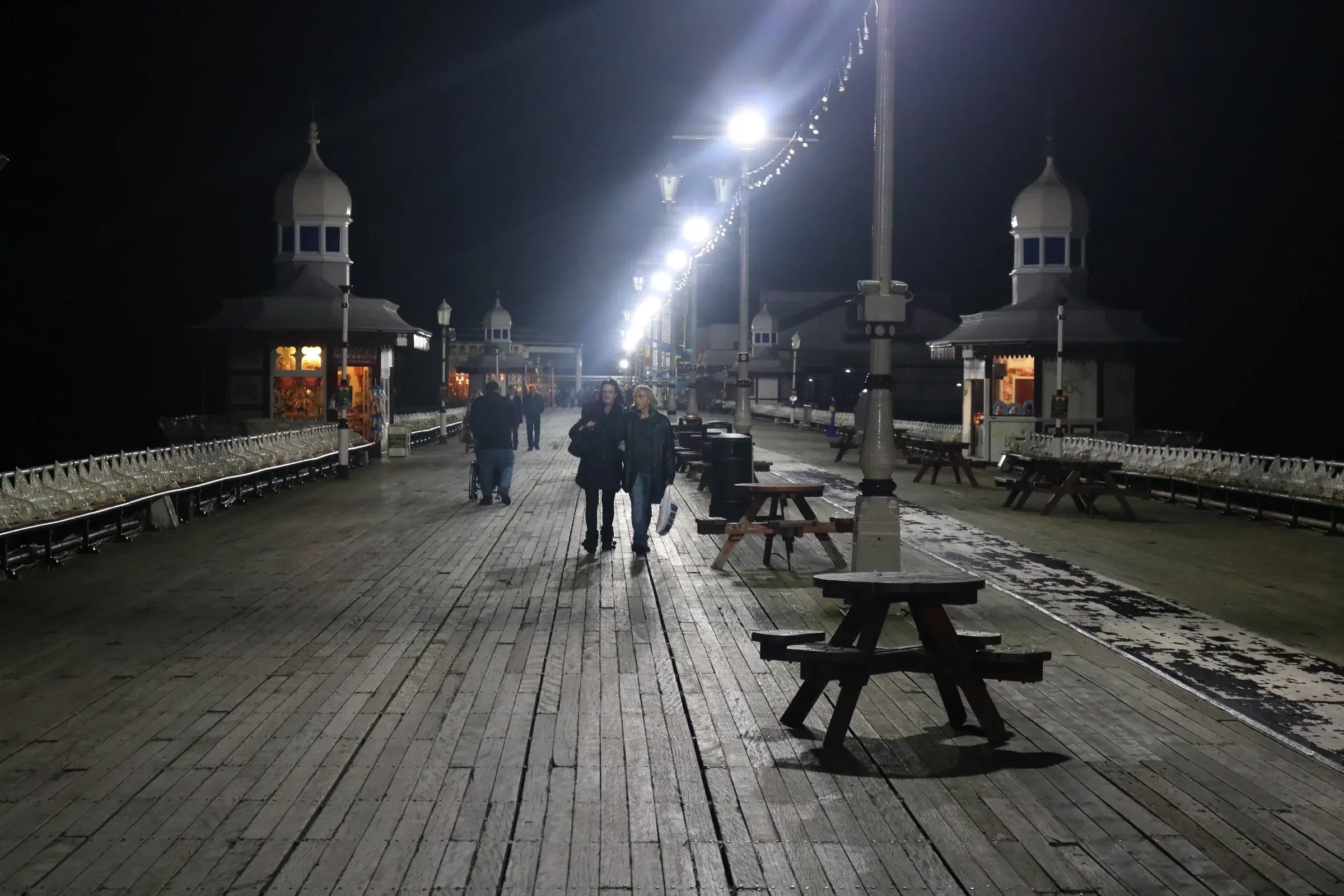 Visitors walking along the illuminated North Pier deck at night